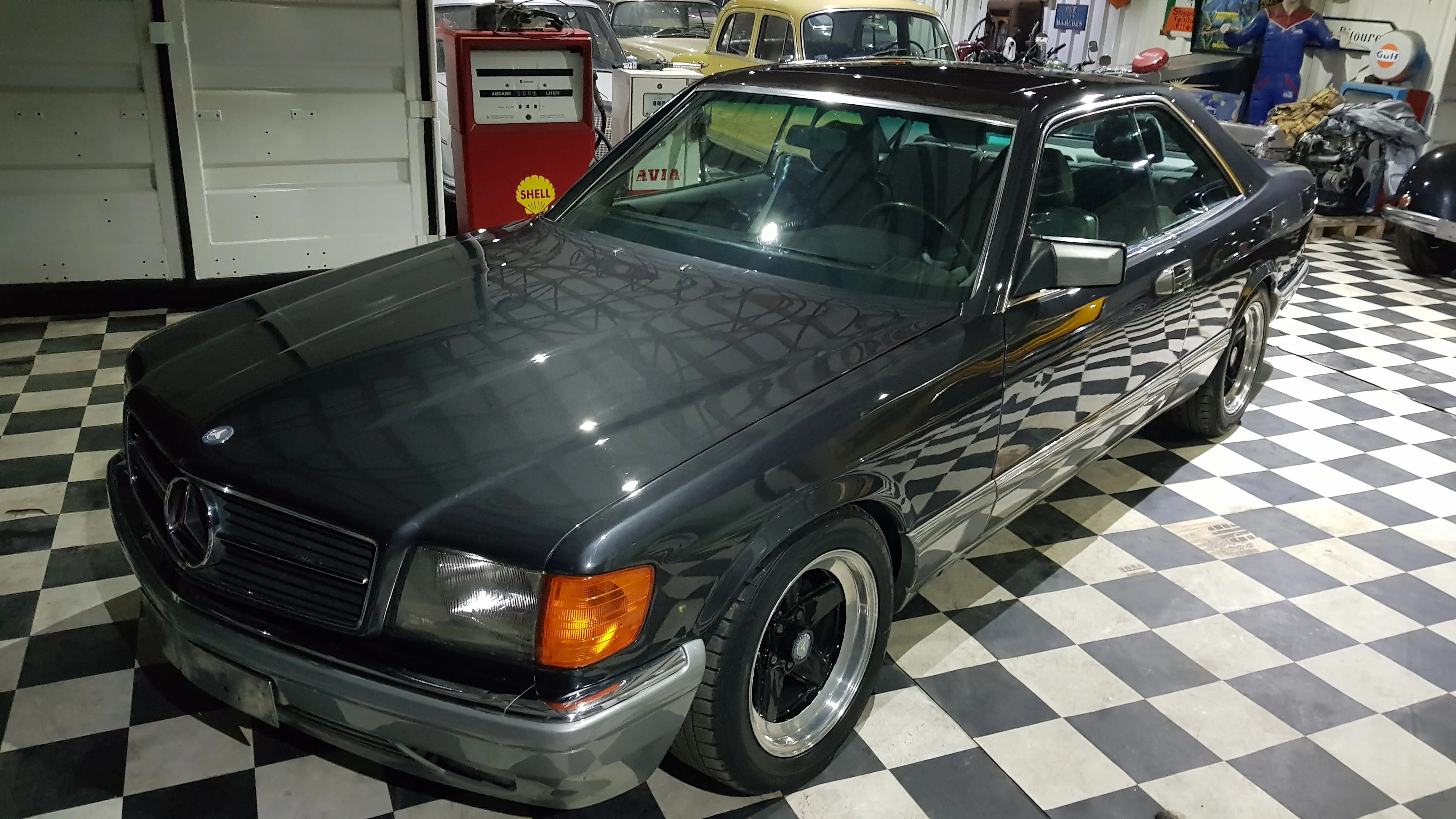Mercedes-Benz W126 SEC w garażu z zabytkowymi pamiątkami motoryzacyjnymi