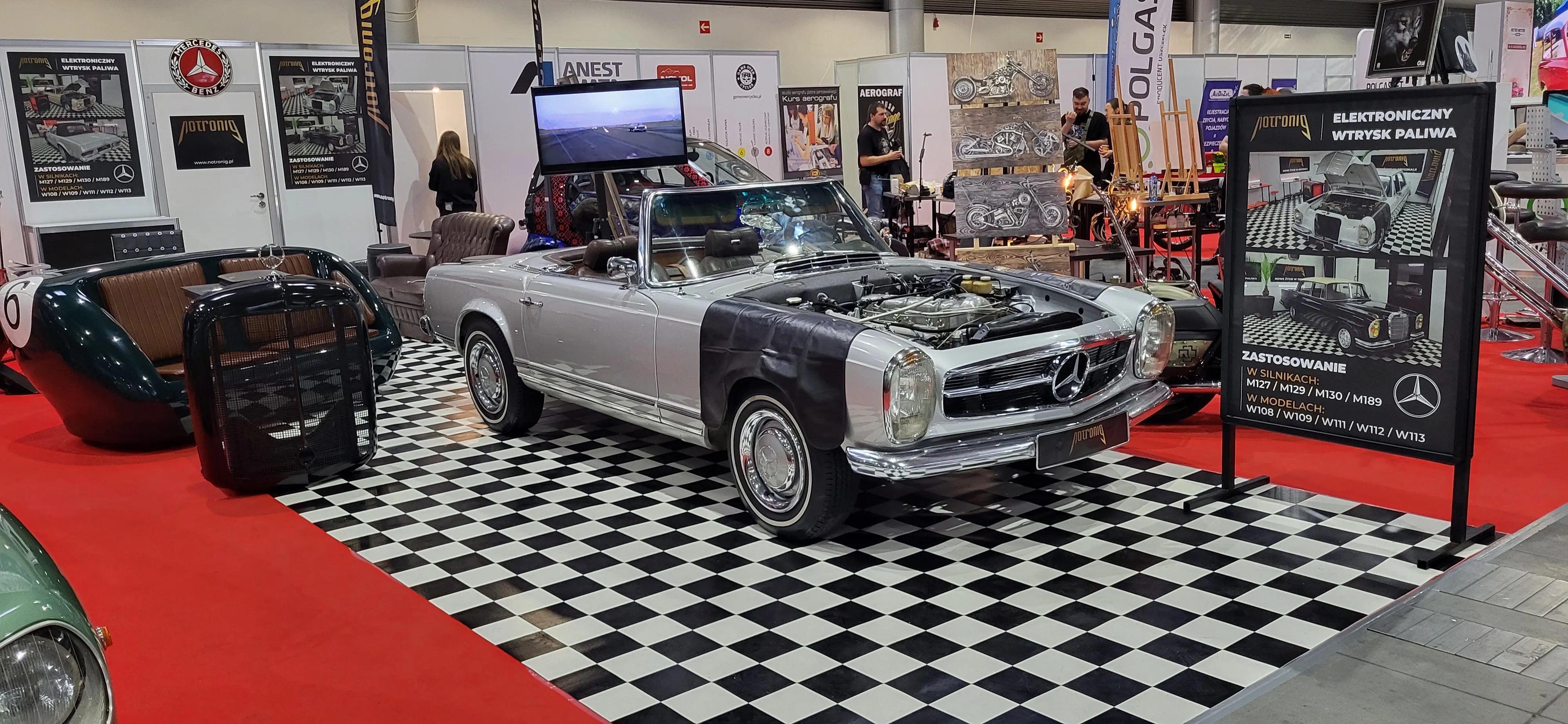 Mercedes-Benz W113 SL (Pagoda) na stoisku NotroniG, maska otwarta, ekran z materiałem promocyjnym w tle